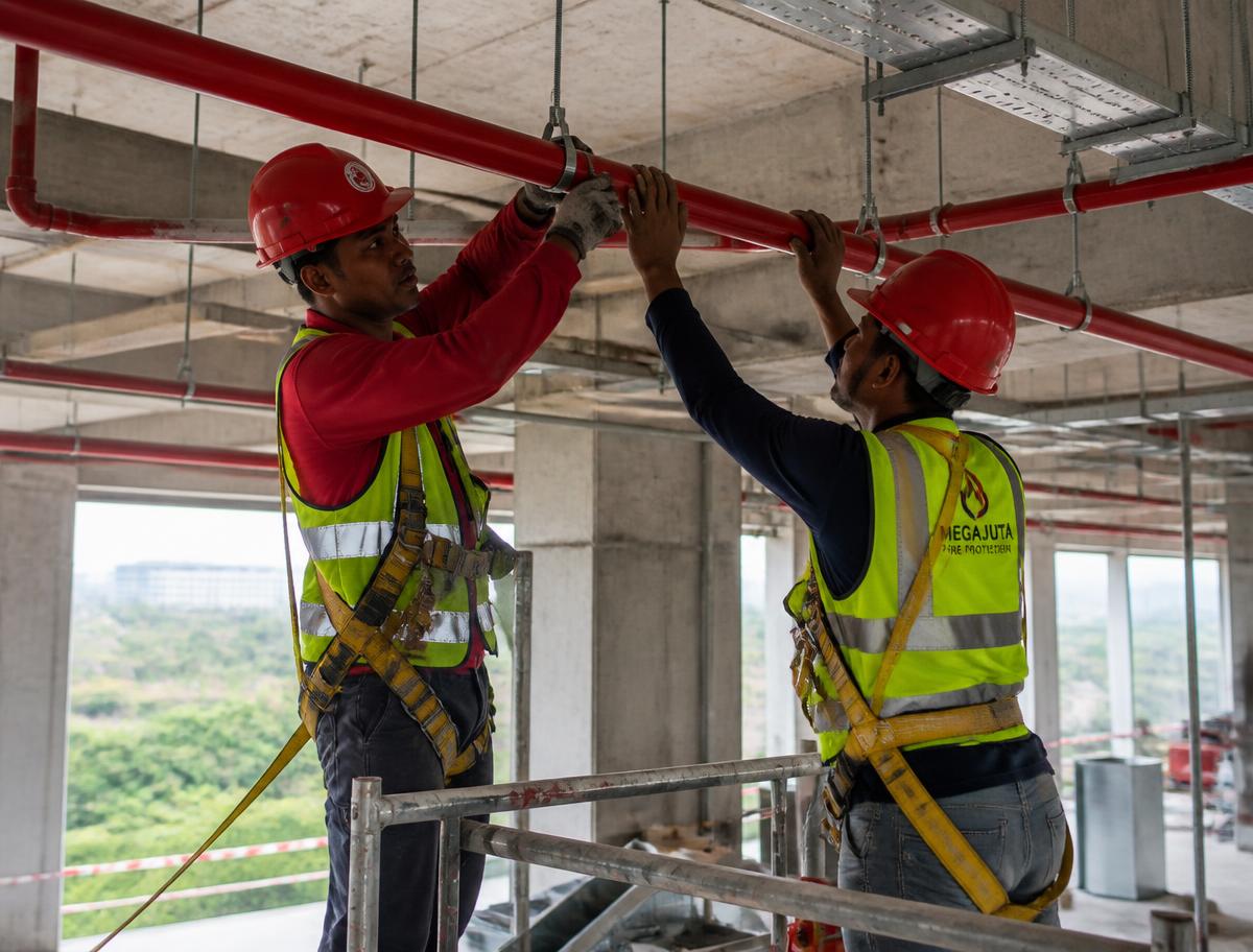 Workers installing fire sprinkler pipework on a construction site