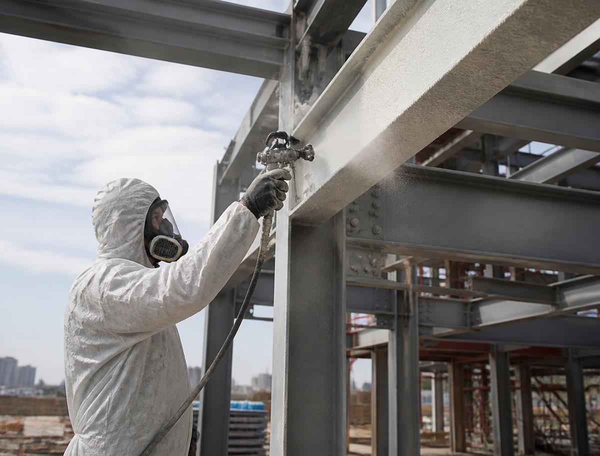 Worker spraying intumescent fire-rated coating onto structural steel